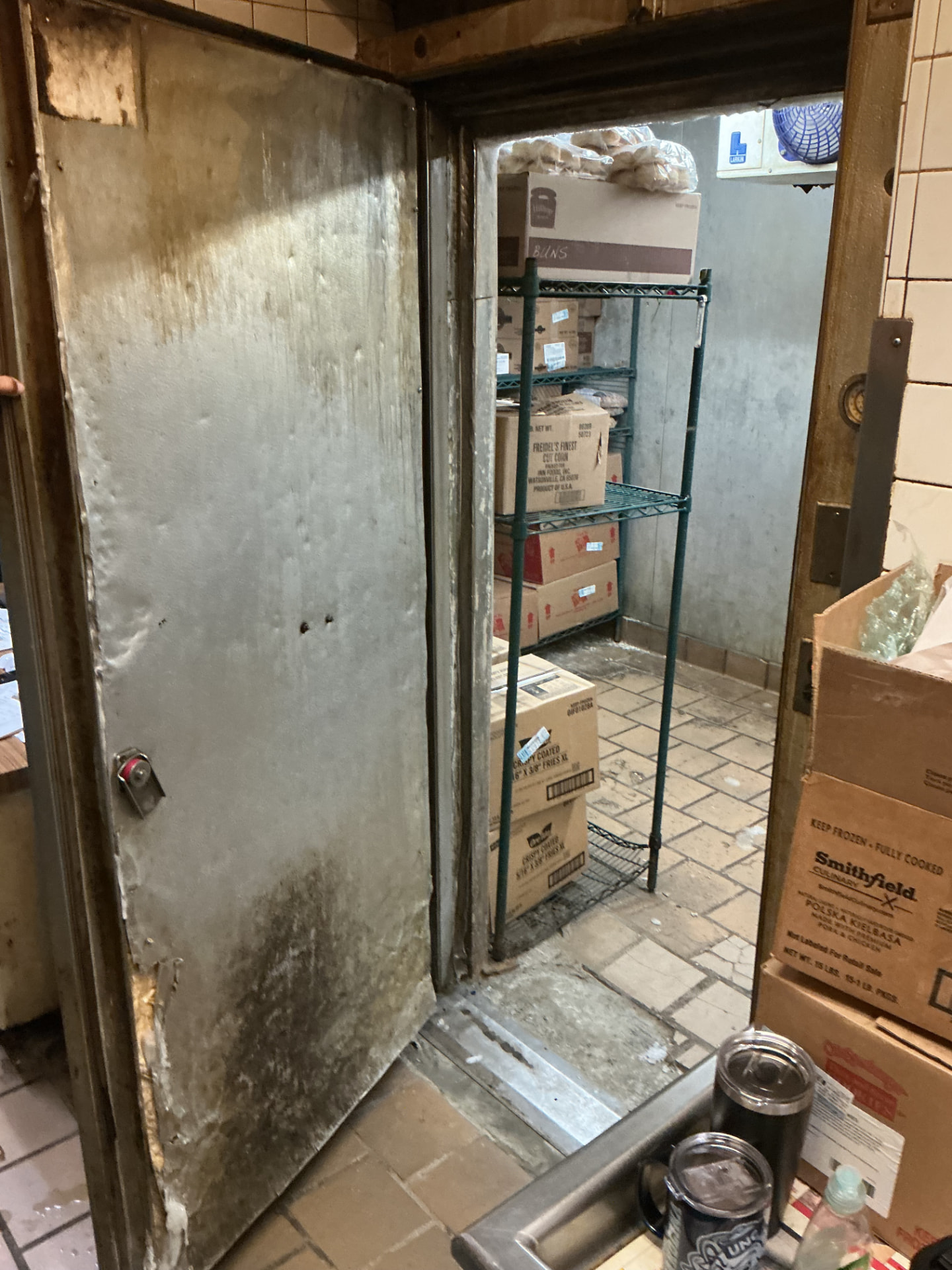 Damaged walk-in freezer door with delaminated panel and bent frame