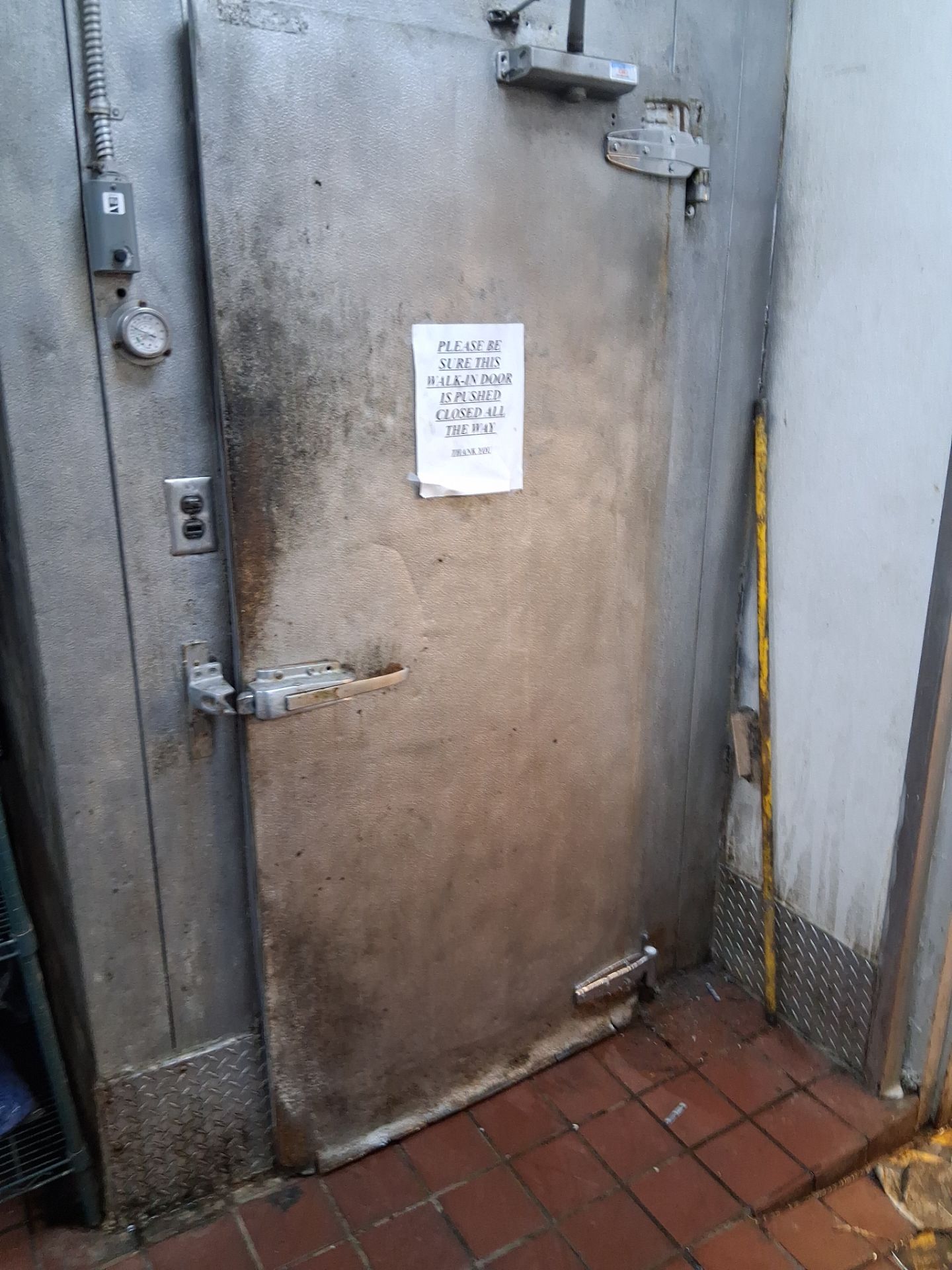Worn walk-in freezer door with a sign asking staff to push it closed